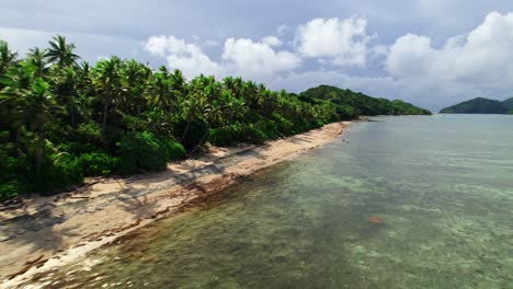 Tropical-island-beachfront,-palm-trees-and-coral-reef-at-high-tide,-Yasawa,-Fiji