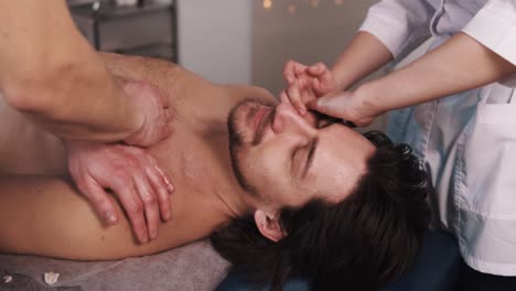Close-up-therapist-is-giving-a-massage-to-a-muscular-man-in-a-beautiful-massage-room-while-he-lies-on-his-back-on-a-massage-table-receiving-a-two-handed-massage