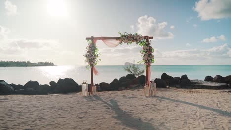 Ein-Mit-Blumen-Bedeckter-Bogen-Für-Eine-Hochzeitsveranstaltung-An-Einem-Sandstrand-Und-Einem-Meer-Im-Sonnenschein