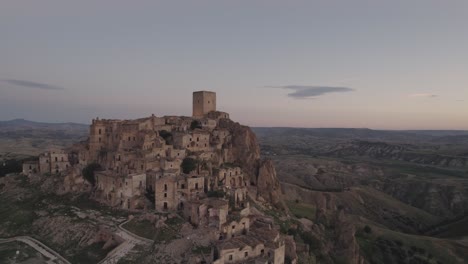 Drone-flying-in-large-circulair-motion-around-the-ruins-of-Craco-on-a-hill-with-the-sunrise-in-the-background-in-4k