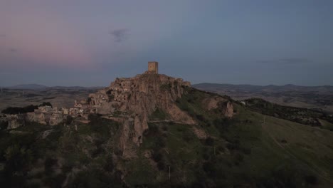 Drone-flying-in-large-circulair-motion-around-the-ruins-of-Craco-on-hilltop-in-the-south-of-Italy-in-the-very-early-morning-light-in-4k