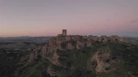 Drohne-Fliegt-In-Großer-Kreisbewegung-Um-Die-Ruinen-Von-Craco-Auf-Einem-Hügel-Im-Süden-Italiens-Und-Endet-Mit-Dem-Sonnenaufgang-In-Der-Ferne-In-4k