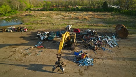 Aerial-view-of-junk-yard-with-a-big-yellow-grapple-excavator-in-Fayetteville,-Arkansas,-USA
