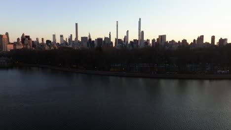 Central-Park-reservoir-and-Manhattan-skyscrapers,-sunset-in-New-York,-USA---descending,-drone-shot