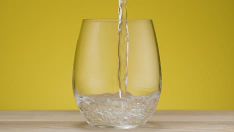 Total-shot-of-a-glas-filling-with-sparkling-water,-isolated-yellow-backdrop