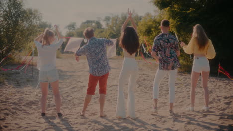 Young-male-and-female-friends-dancing-at-beach