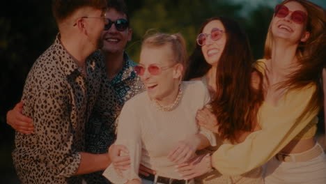 Young-woman-wearing-hat-and-sunglasses-with-friends-embracing-her