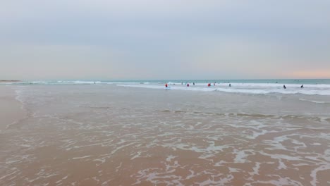 Low-aerial-dolly-over-low-tide-waves-as-surfers-carry-boards-walk-to-surf-break
