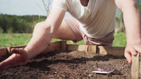 Man-Digging-Soil-To-Plant-Seeds-On-Wooden-Planter