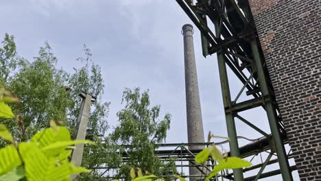 old-industrial-structures-with-pipes,-chimney-and-brick-buildings-overgrown-with-nature