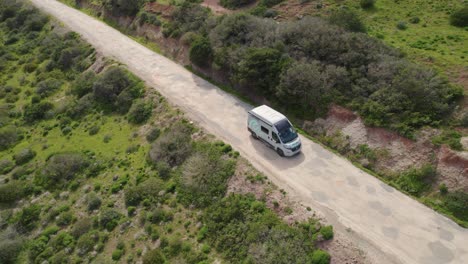 Camper-van-driving-along-an-old-road-between-hills-covered-with-bushes-and-greenery