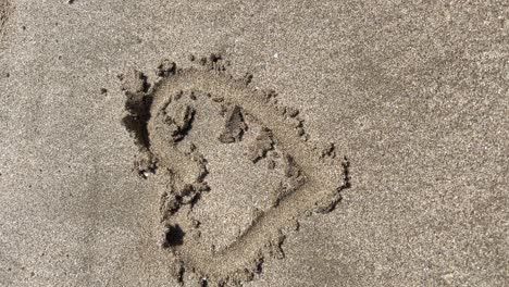 vertical-tracking-shot-of-a-heart-drawn-in-the-wet-sand-of-the-beach