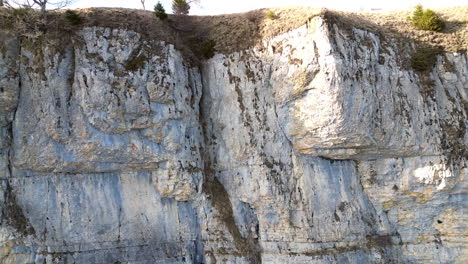 Aerial-ascent-closeup-of-rock-cliff-face-and-meadow-above,-Wandfluh-Solothurn,-Switzerland