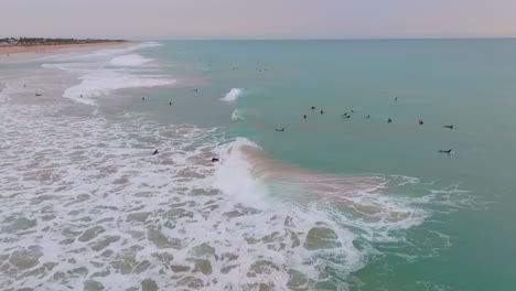 Waves-crashing,-spread-beautiful-ocean-mist-over-surfers-at-sunset,-aerial-orbit