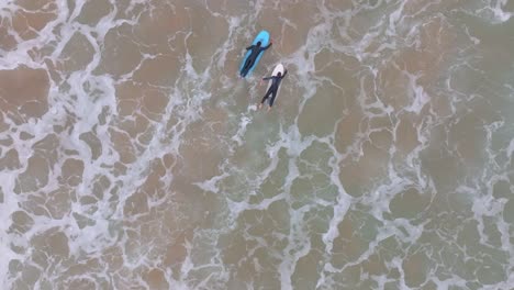 Top-down-tracking-view-of-two-longboard-surfers-paddling-out-to-catch-ocean-wave