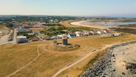 Circling-drone-flight-centered-around-historic-Martello-Tower-on-coastal-promontory-showing-bays-and-promontory-at-low-tide-with-boats-at-anchor-and-drying-on-stunning-golden-beaches