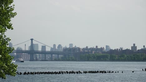 A-river-cruise-ship-catamaran-powers-forward,-gliding-past-the-iconic-Brooklyn-Bridge-on-New-York's-East-River