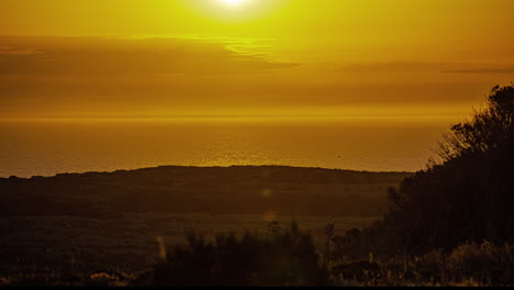 Beautiful-timelapse-of-sun-rising-over-a-beach-with-green-vegetation-along-the-coastline-during-morning-time