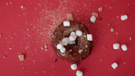 Decorating-chocolate-donut-with-white-marshmallows,-red-table-background,-slowmo