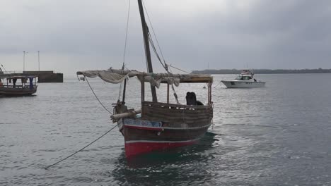 Barco-Dhow-Anclado-En-La-Bahía-Con-El-Hombre-Vertiendo-Agua-Del-Barco-Al-Océano