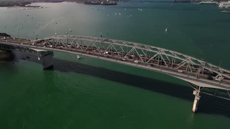 Fahrzeuge-überqueren-Den-Hafen-Von-Waitemata-über-Die-Auckland-Harbour-Bridge-In-Auckland,-Neuseeland,-Mit-Booten,-Die-Auf-Türkisfarbenem-Wasser-Treiben