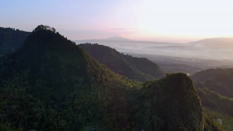 Cinematic-drone-shot-of-green-mountain-hills-in-the-morning-with-fog-in-the-valley-at-sunrise---Asia,-Indonesia