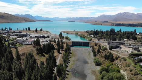 Drone-Aerial-View-of-Lake-Tekapo-Village,-Dam-and-River-Watercourse,-New-Zealand