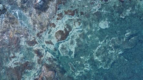 Unique-rock-formation-under-the-sea-with-waves-crashing-|-Steady-aerial-shot-over-clear-turquoize-water-|-4K