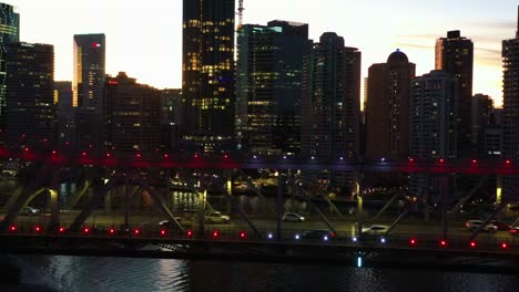 Beleuchtetes-Stadtbild-Der-Innenstadt,-Denkmalgeschützte-Story-Brücke-Mit-Viel-Verkehr,-Der-In-Der-Abenddämmerung-Den-Fluss-überquert,-Brisbane-City,-Queensland,-Filmische-Kamerafahrt