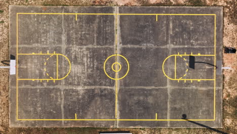 Aerial-top-down-shot-of-old-empty-amateur-basketball-court-surrounded-by-sandy-desert,America