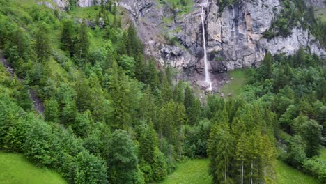 Descending-backwards-Aerial-Drone-view-of-Almenbachfall-waterfall-in-Kandertal-flowing-among-pine-trees-and-alpine-rocks,-Kandersteg-Berner-Oberland-Switzerland