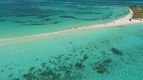 Drone-pan-right-tropical-sandbar,-people-walking-along-white-sand,-sea-water-texture