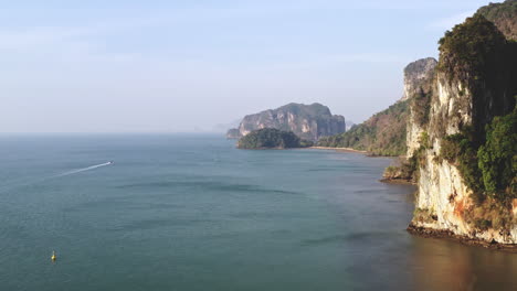 Massive-coastal-limestone-cliffs-in-Andaman-sea,-boat-cruising-below