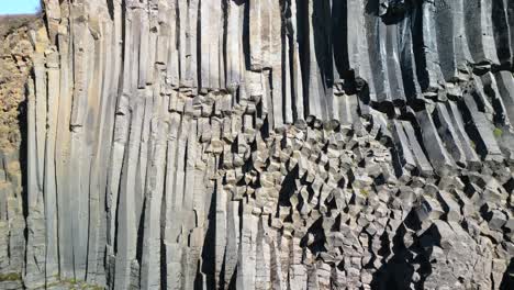 Aerial-drone-tilt-up-shot-flying-over-rocky-column-shaped-Studlagil-Canyon-in-east-Iceland,-Europe-on-a-sunny-day
