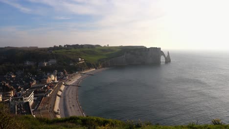 Aerial-wide-shot-of-beautiful-beach-in-Etretat-and-famous-white-chalk-rock-formation-at-coast-in-background-during-sunset-time