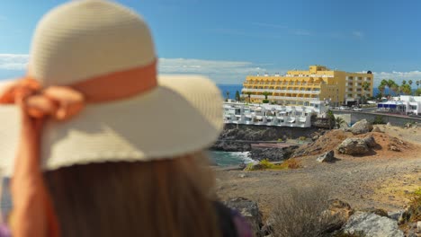 Rear-close-up-shot-of-woman-on-vacation-wear-summer-hat,-looking-at-sea-resort