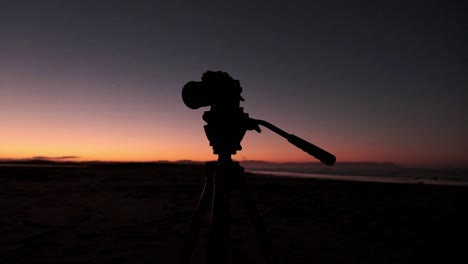 Silhouette-Einer-Digitalkamera-Auf-Einem-Stativ-Im-Morgengrauen-Am-Strand