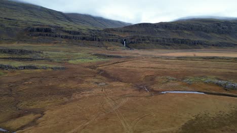 Paisaje-Islandés-árido-Con-Cascada-En-Las-Montañas,-Inclinación-Aérea-Hacia-Abajo