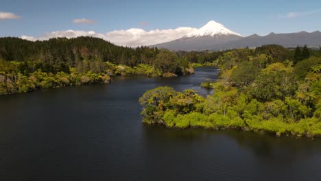 Stunning-aerial-scenic-over-native-bush-and-lake,-view-of-Taranaki-volcano,-famous-tourist-destination-in-New-Zealand