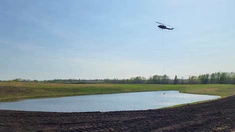 Helicopter-bucket-collecting-water-from-nearby-lake-during-wildfires,-Alberta,-Canada