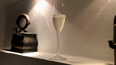 Elegante-Präsentation-Von-Funkelndem-Champagnerglas-In-Der-Gemütlichen-Ecke-Eines-Wandregals-Neben-Rustikalem-Altem-Eisen