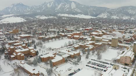 Cars-driving-on-snowy-road-over-University-of-Colorado-Boulder-Campus-during-misty-winter-day-in-Colorado---Aerial-Drone-backwards-flight