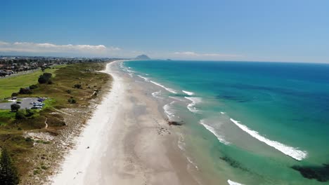 Papamoa-Beach-aerial-pull-back,-Mount-Maunganui-on-horizon,-beautiful-summer-sunny-day,-New-Zealand