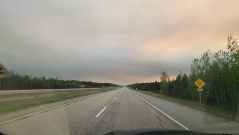 Dashcam-driving-alone-along-a-rural-road-at-sunset,-pink-orange-pastel-clouds,-end-of-day,-scenic-drive,-nobody-on-the-freeway,-empty,-solitude