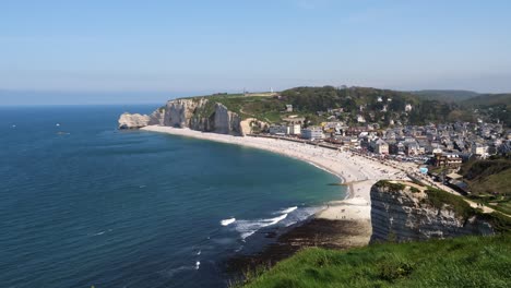 Aerial-Wide-shot-of-Etretat-City-with-sandy-beach-and-sea-cliffs-in-background-during-sunny-day-in-France---Picturesque-landscape-with-blue-sky---panning-shot
