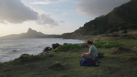 Mujer-Sentada-En-La-Playa-Rocosa-Leyendo-Un-Libro-En-Kindle-En-La-Isla-De-Con-Dao,-Vietnam