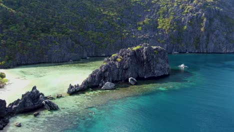 Barco-Turístico-Filipino-Atracado-Junto-A-Una-Montaña-De-Piedra-Caliza-Irregular-Y-Aguas-Cristalinas-De-La-Bahía-De-La-Isla-Tapiutan