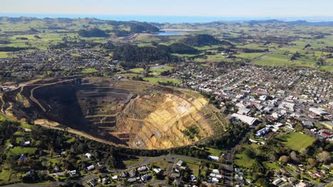 Gold-mining-pit-in-the-middle-of-Waihi-town,-aerial-reveal-of-New-Zealand-cityscape-and-coastal-scenery