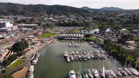 Drone-fly-over-docked-boats-in-Hatea-river,-tilt-up-Whangarei-cityscape,-New-Zealand