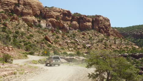 SUV-vehicle-drives-dusty-gravel-road-winding-along-rugged-Moab-canyons